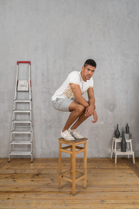 Homme aux bras croisés accroupi sur un tabouret