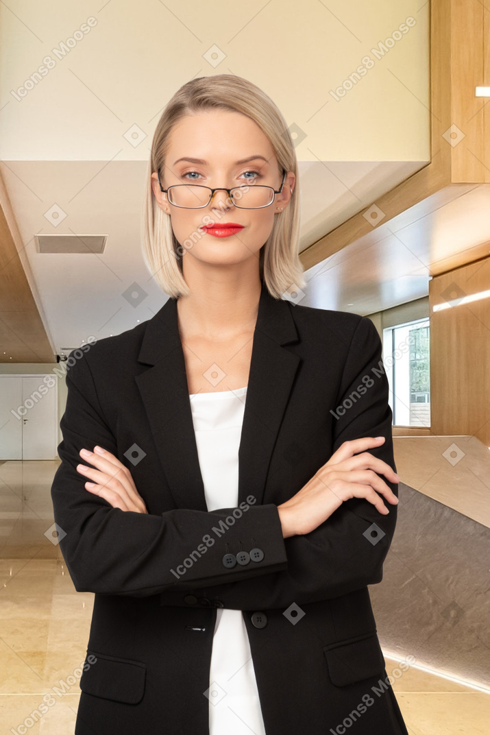 A woman in a suit and glasses standing with her arms crossed