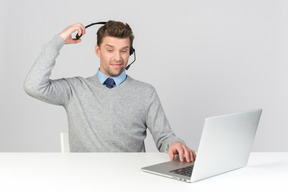 Call center agent pulling off his headset while working on computer