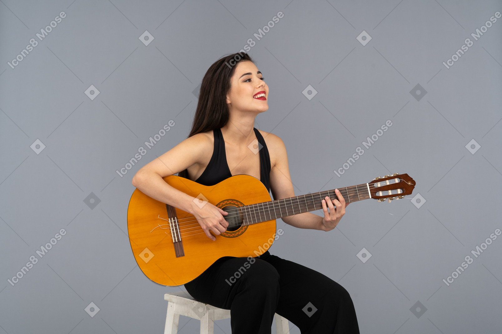 Vista de três quartos de uma jovem sorridente sentada de terno preto tocando violão