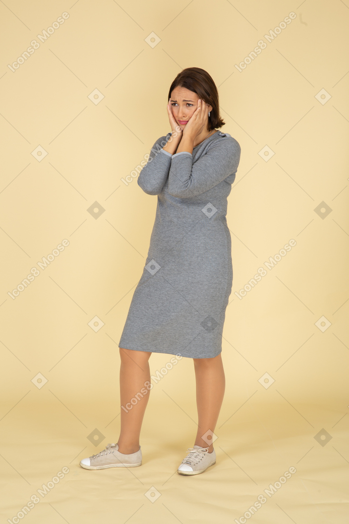 Vista frontale di una donna triste in abito grigio che le tocca il viso
