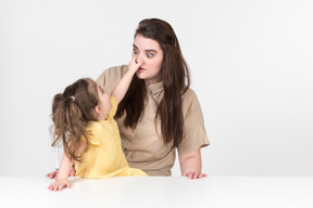 Малыш девочка сидит за столом и держит нос своей матери