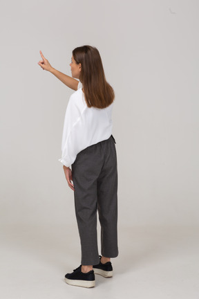 Vista posterior de una joven en ropa de oficina apuntando con el dedo hacia arriba