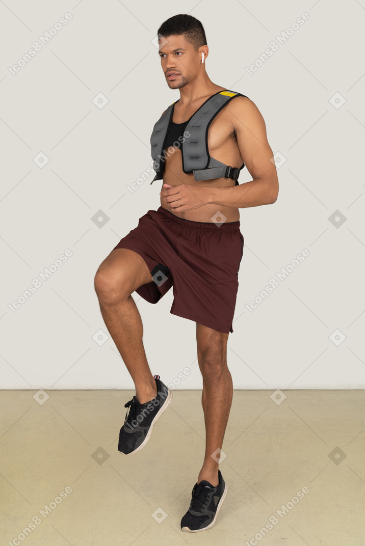 Bare chested young man in sport shorts and training vest lifting a leg
