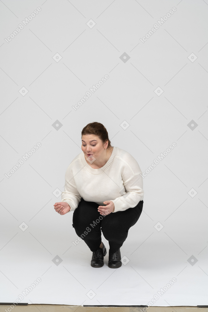 Front view of a plus size woman in white sweater squatting