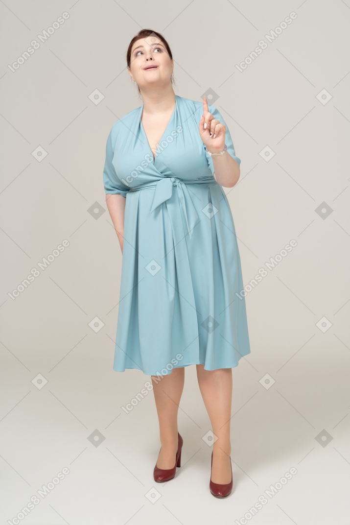 Vista frontal de uma mulher de vestido azul apontando para cima com um dedo