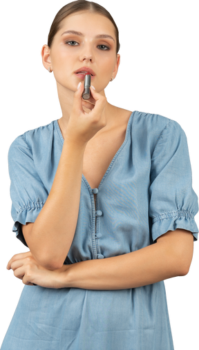 Vista frontale di una giovane donna in abito blu che applica un rossetto