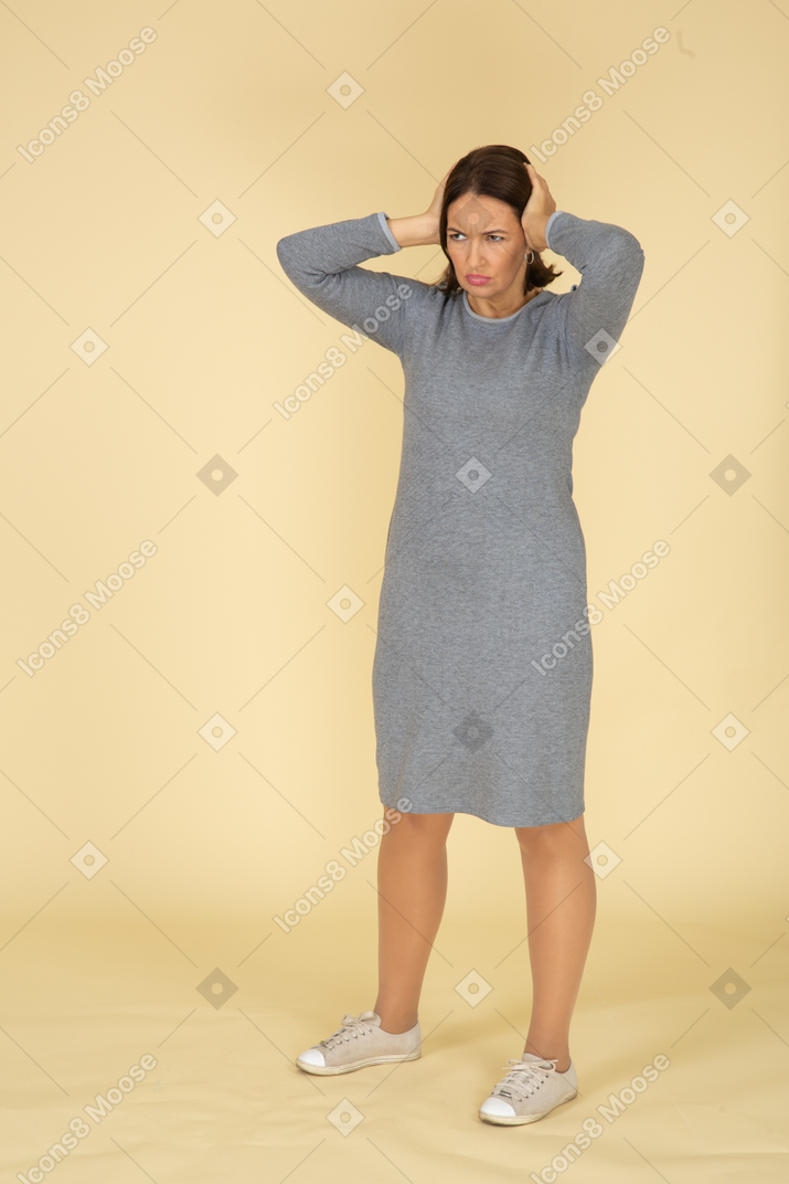 손으로 귀를 막는 회색 드레스를 입은 여성의 전면 모습