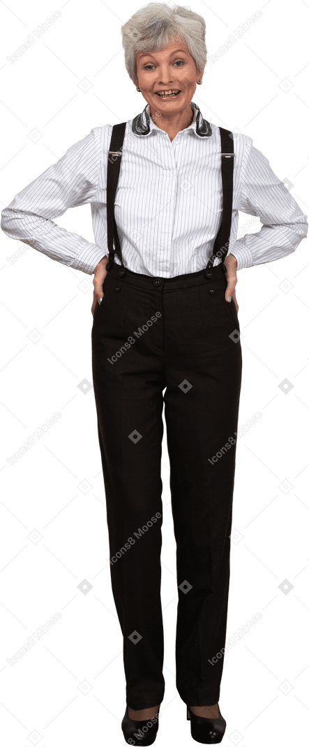 A smiling old woman dressed in trousers and suspenders smiling and putting hands in hips