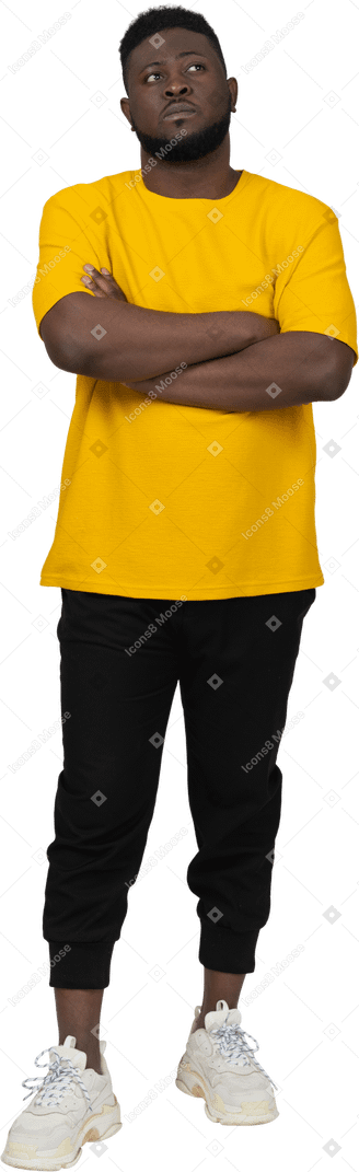 노란색 티셔츠를 입고 팔짱을 끼고 있는 의심스러운 젊고 검은 피부의 남자