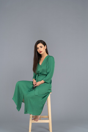 Pleine longueur d'une jeune femme en robe verte assise sur une chaise tout en tenant la clarinette