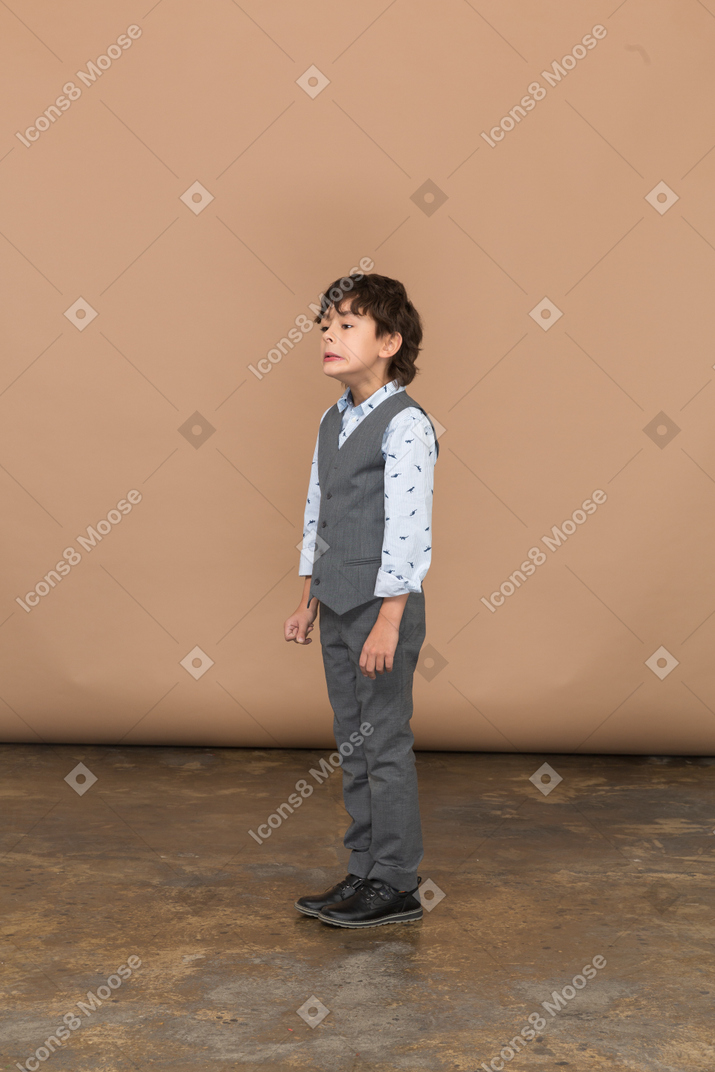 Vista lateral de um menino de terno cinza fazendo caretas