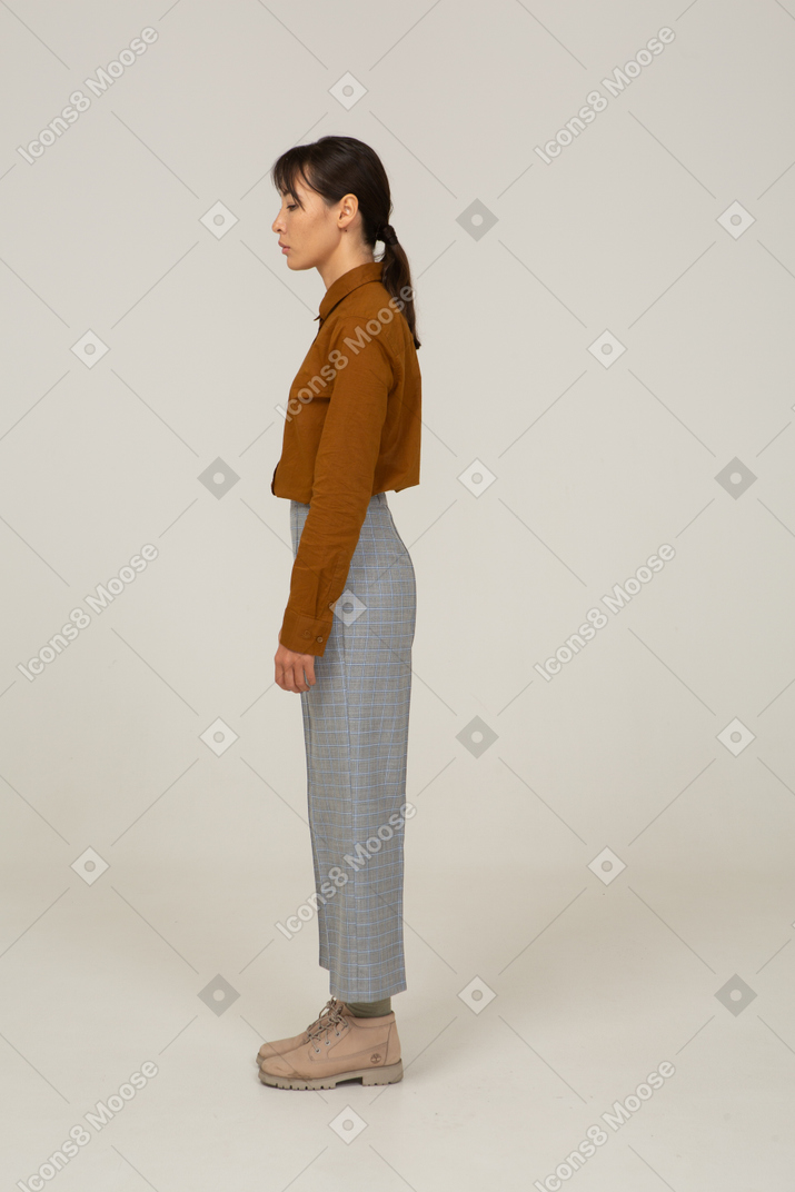 Vista lateral de uma jovem mulher asiática de calça e blusa parada