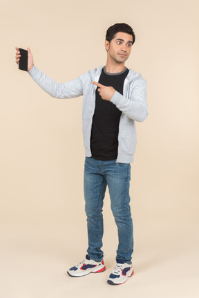 Young caucasian man pointing at smartphone he's holding