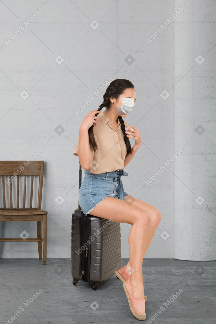 Woman in face mask sitting on a suitcase