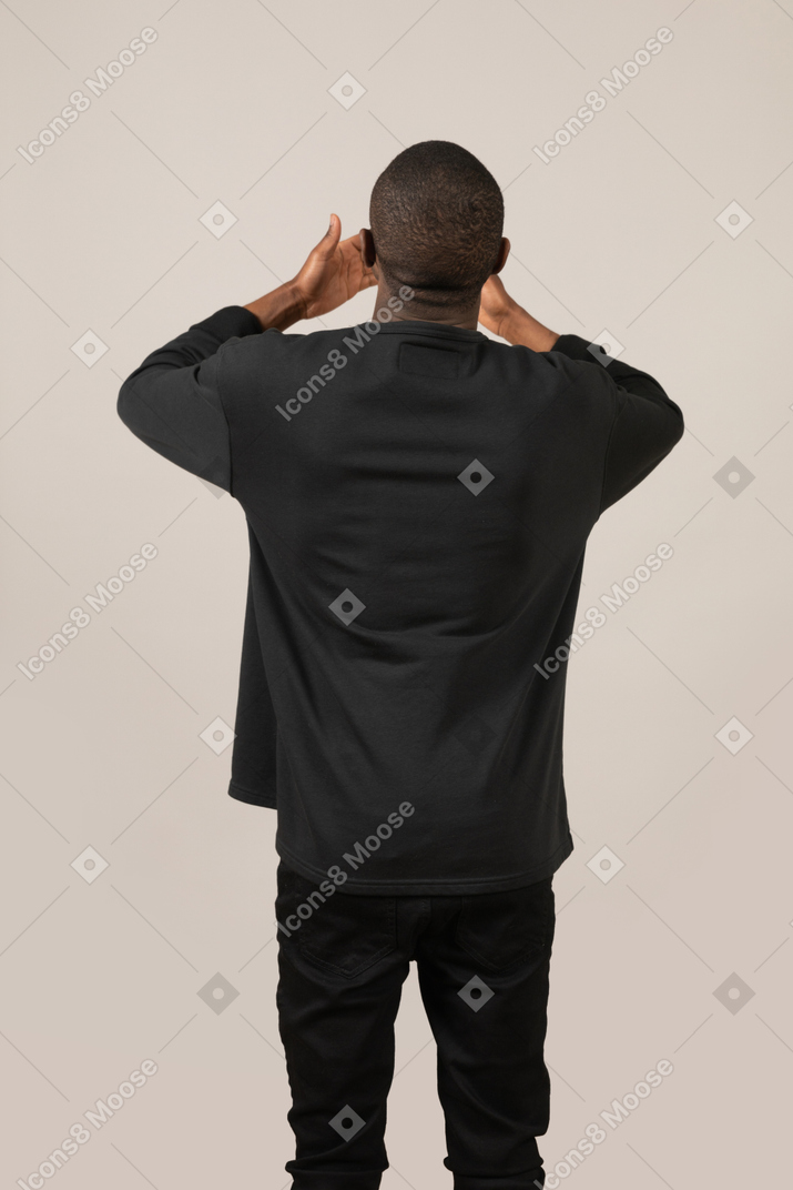 Back view of young man standing with hands on head