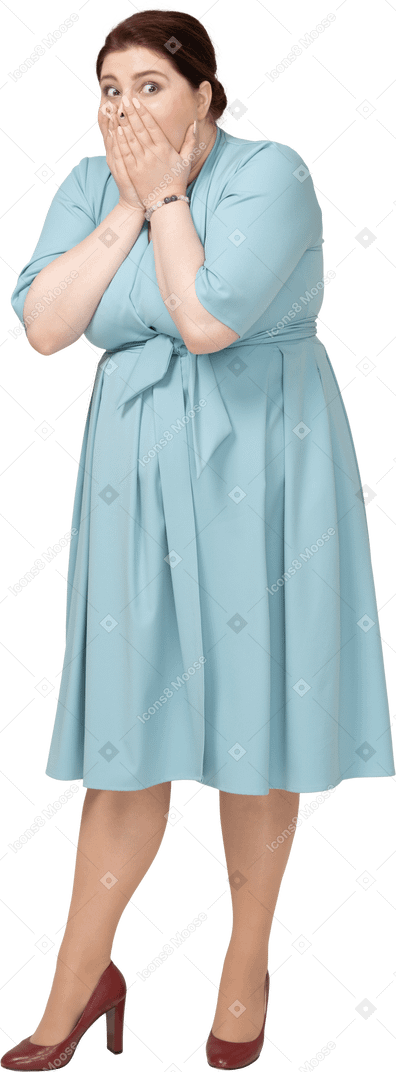 Vista frontal de una mujer sorprendida en vestido azul cubriendo la boca con las manos