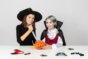 Boy in vampire costume and mom in witch costume carving a pumpkin