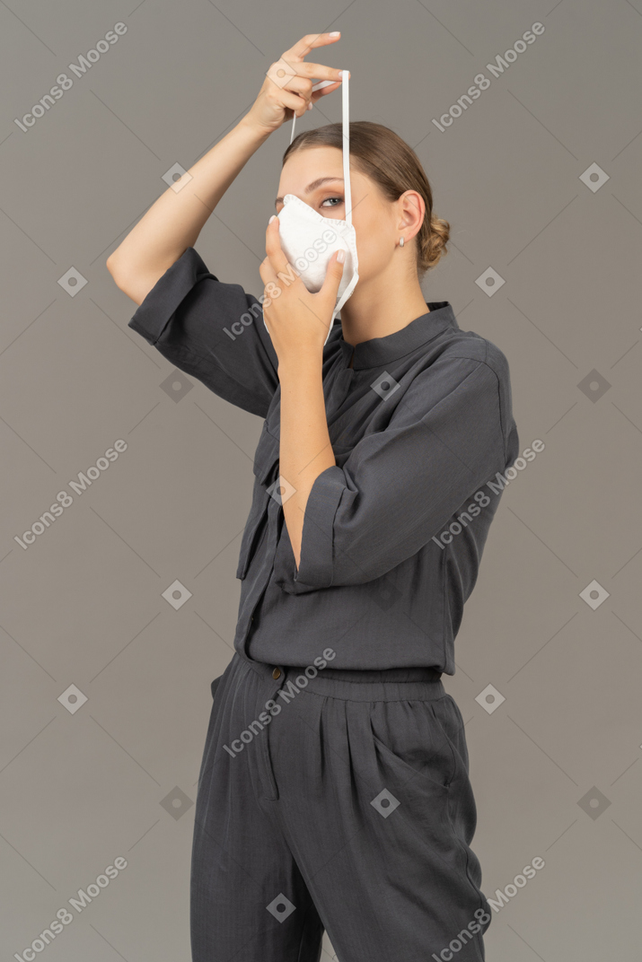 Woman in gray coveralls putting on a respirator