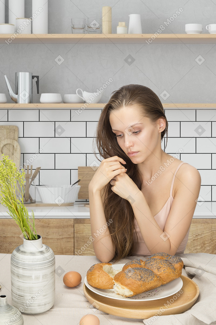 Young woman sitting on the kitchen counter and eating bread