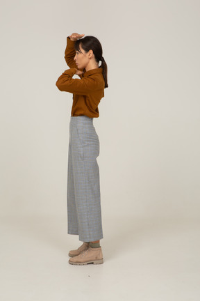 Vista lateral de uma jovem mulher asiática de calça e blusa mostrando o tamanho da cabeça