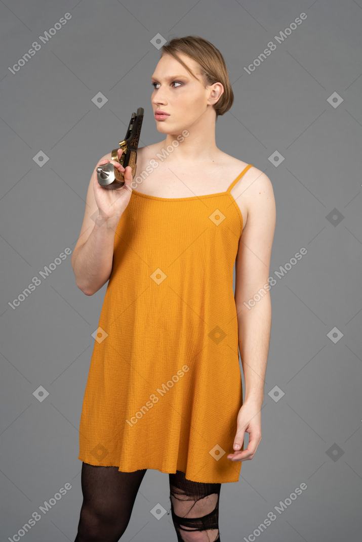 Portrait of a young queer person in orange dress carrying a gun