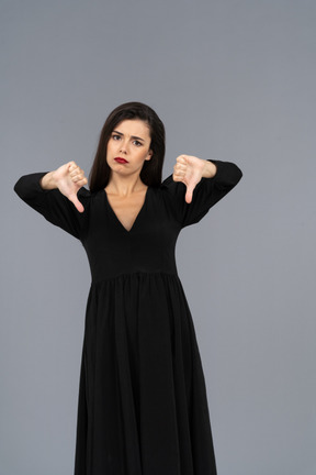 Front view of a displeased young lady in black dress putting thumbs down