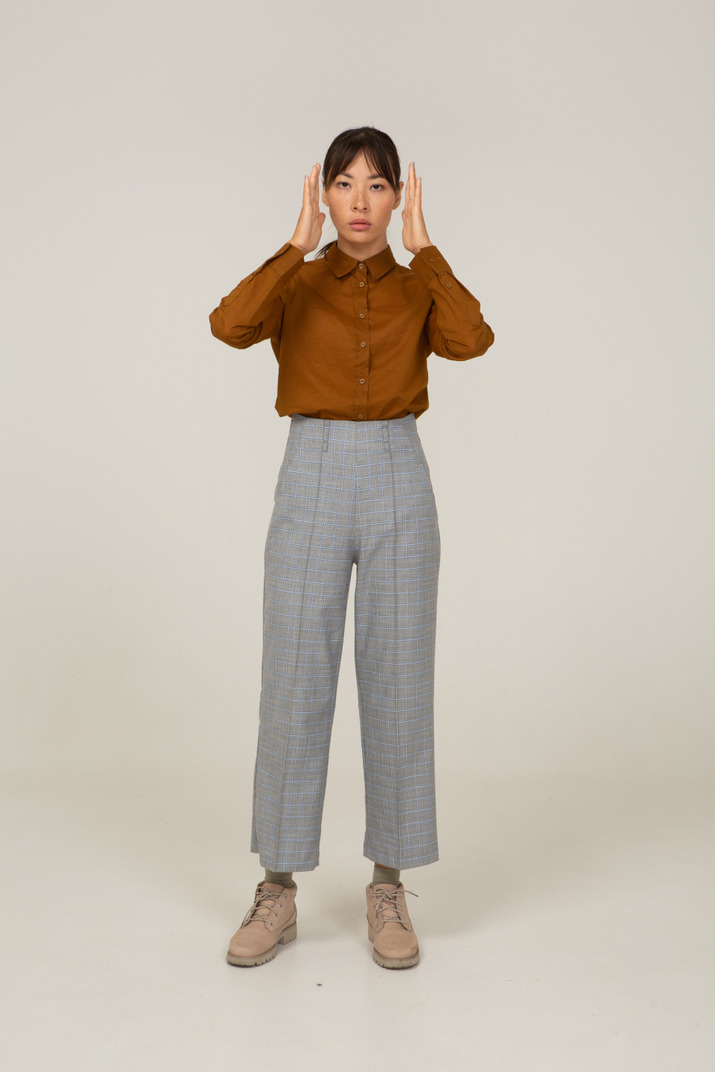Front view of a young asian female in breeches and blouse raising hands