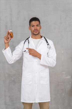 Male doctor in lab coat pointing at pill bottle