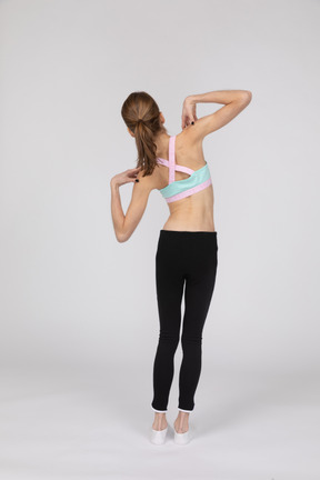 Vista traseira de uma adolescente em roupas esportivas tocando seus ombros e inclinando-se para a esquerda