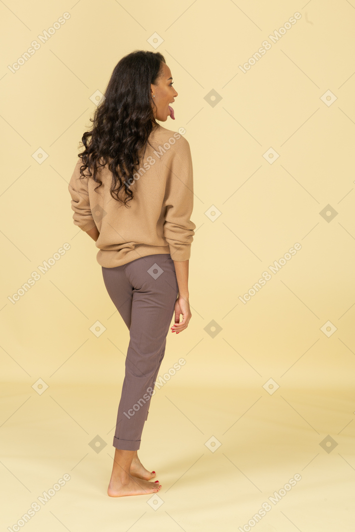 Vista traseira a três quartos de uma jovem mulher com roupas casuais, mostrando a língua