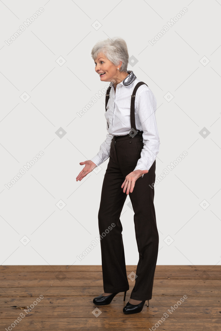 Трехчетвертный вид улыбающейся жестикулирующей старушки в офисной одежде