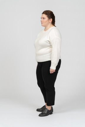 Женщина больших размеров в белом свитере стоит в профиль