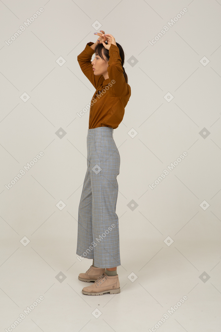 一位身着马裤和衬衫的年轻亚洲女性举手的侧视图