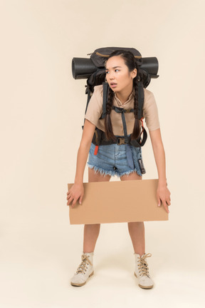 Troubled looking young female hitchhiker holding paper card