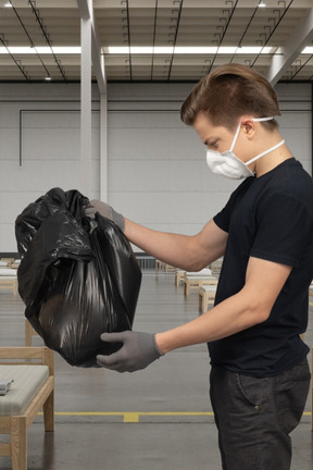 A man wearing a face mask and gloves holding a black bag