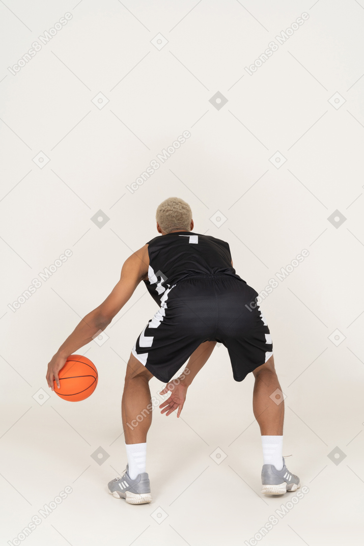 Vista traseira de um jovem jogador de basquete fazendo dribles