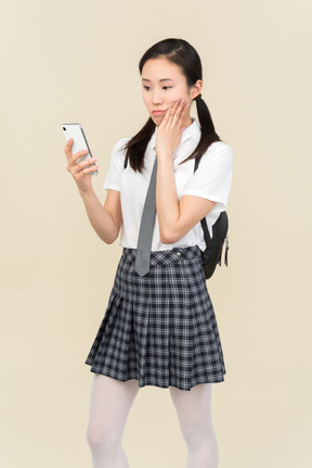 Ragazza della scuola asiatica pensieroso guardando il telefono