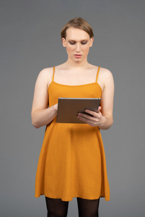 Вид спереди на молодого квир-человека в оранжевом платье с помощью планшета