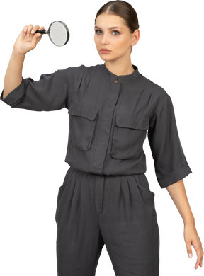 Front view of young woman in a jumpsuit holding a magnifying glass