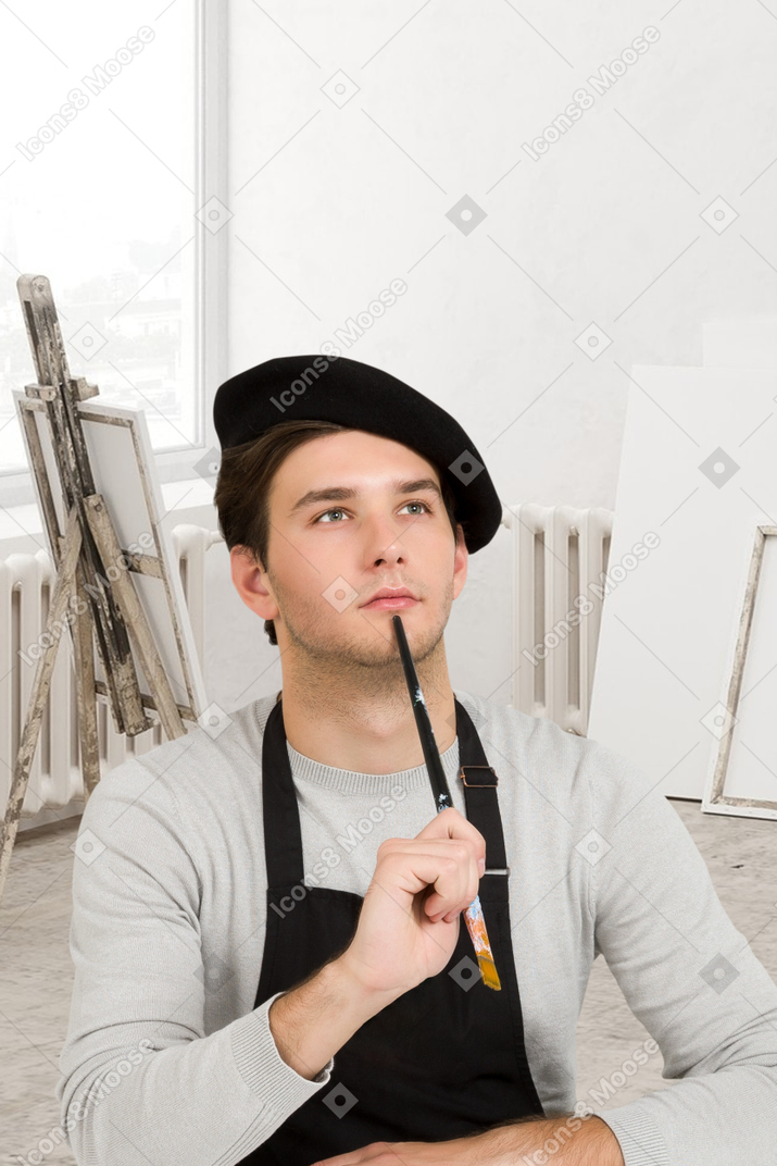 A thoughtful male artist holding paint brush in a studio