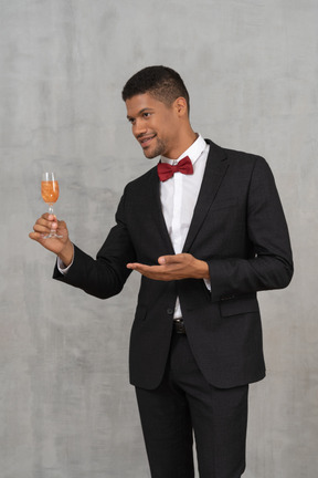 Young man looking aside and showing a champagne glass