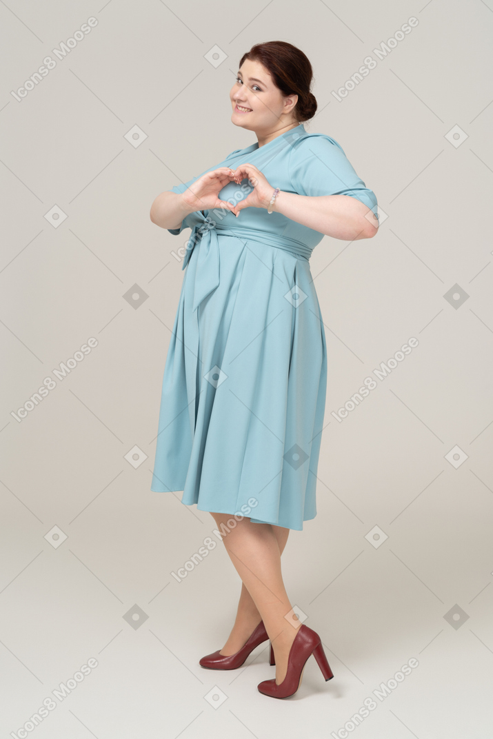 Side view of a woman in blue dress showing heart gesture