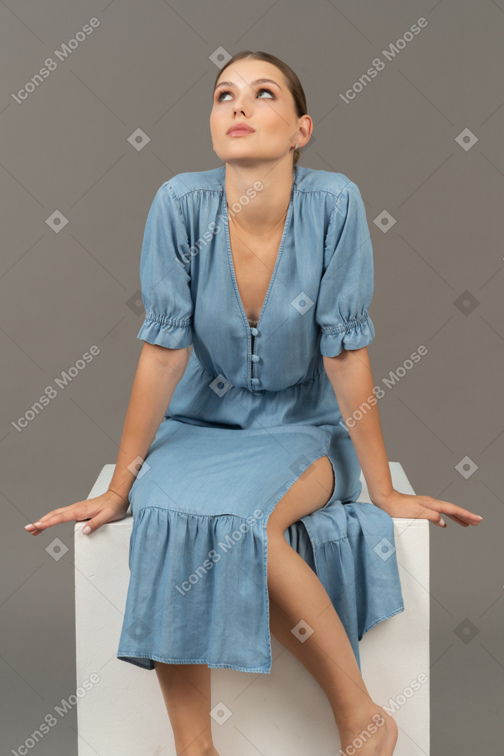 立方体に座って見上げる若い女性の正面図