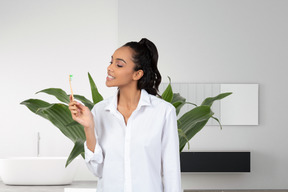 A woman holding a toothbrush in front of a plant