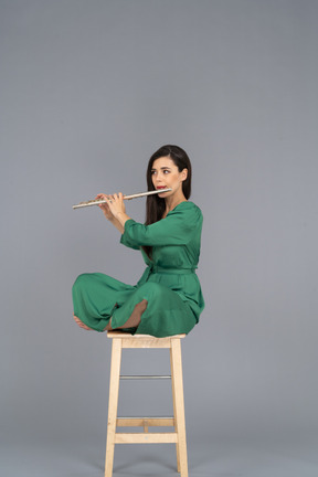 Full-length of a young lady playing the clarinet sitting with her legs crossed on a wooden chair