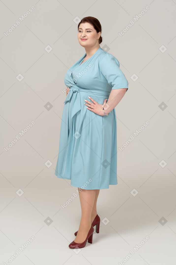 엉덩이에 손을 대고 포즈를 취하는 파란 드레스를 입은 여자의 측면보기