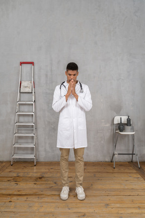 一位忧心忡忡的年轻医生站在一间带梯子和椅子的房间里的前视图