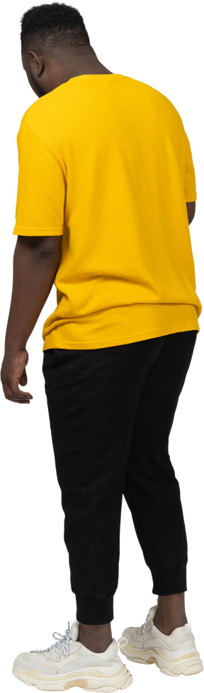 Three-quarter back view of a young dark-skinned man in yellow t-shirt standing still
