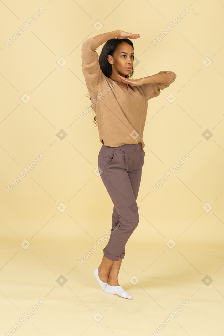 Вид в три четверти темнокожей молодой женщины, держащей руки горизонтально возле ее лица
